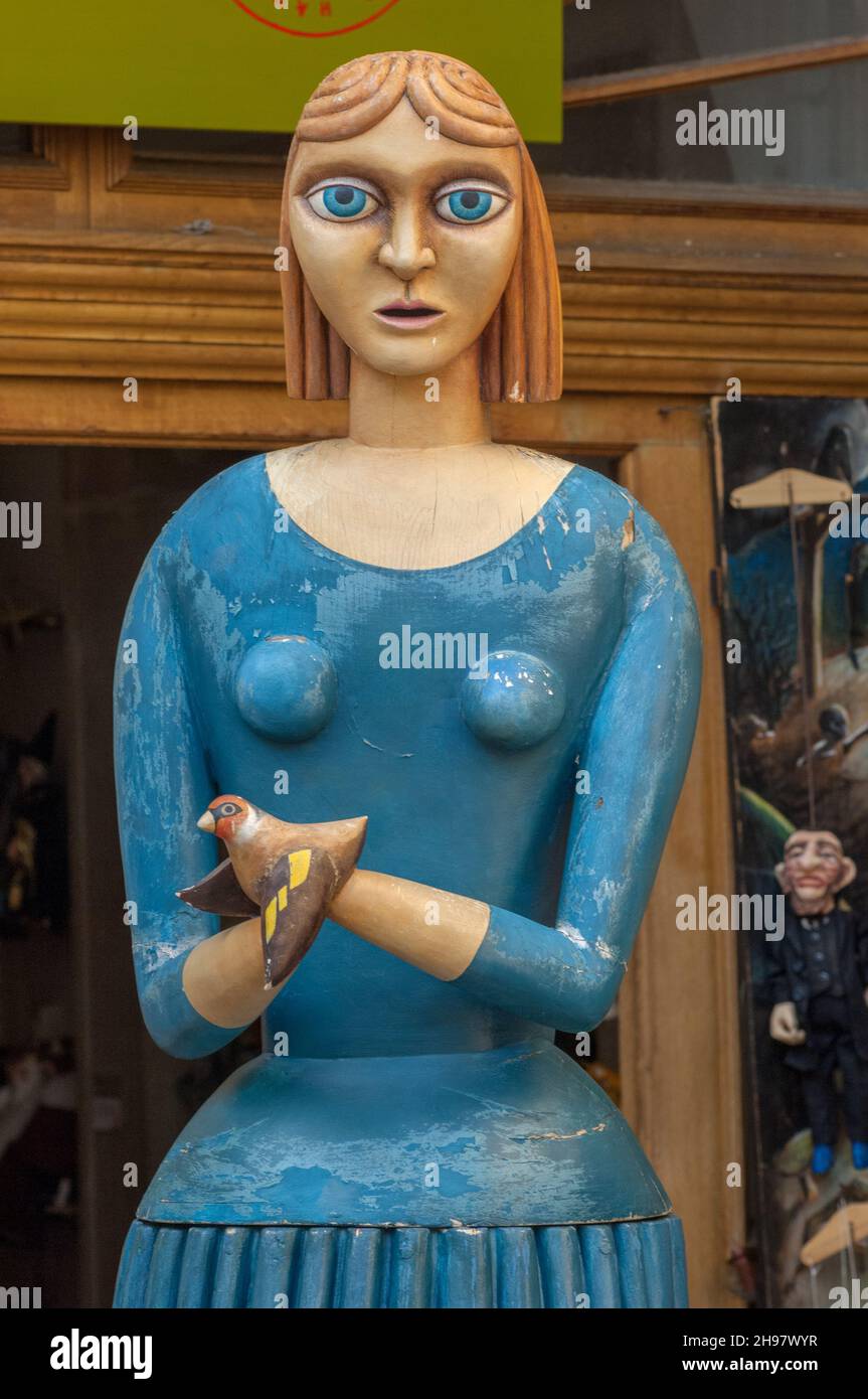 Un gran maniquí de madera de una mujer vestido de azul con un pájaro en la puerta de una tienda de marionetas en Malá Štupartská, en el casco antiguo de Praga. Foto de stock
