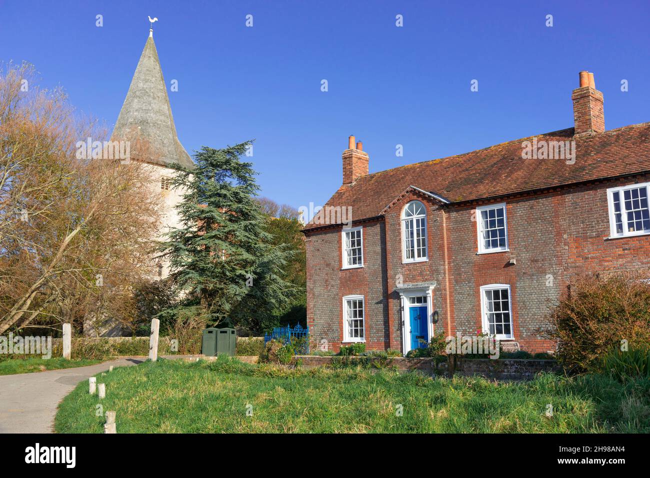 El pueblo verde en Bosham, que tiene vistas al mar, mostrando el grado II listado Brook House construido en 1743 y la iglesia de la Santísima Trinidad, Brook Lane, Bosham, Reino Unido Foto de stock