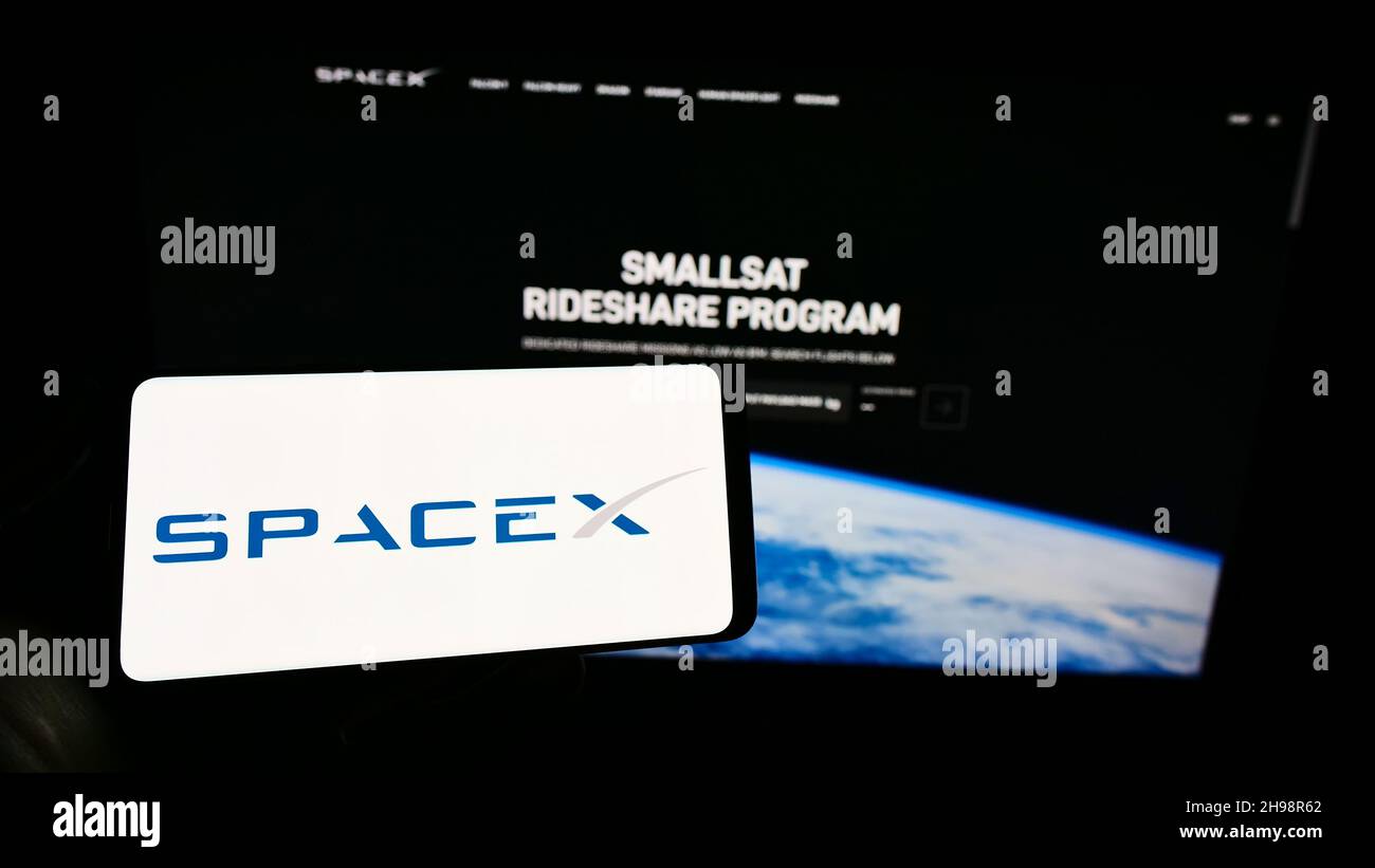 Persona que sostiene el teléfono móvil con el logotipo de la empresa Space Exploration Technologies Corp. (SpaceX) en la pantalla frente a la página web. Enfoque en la pantalla del teléfono. Foto de stock