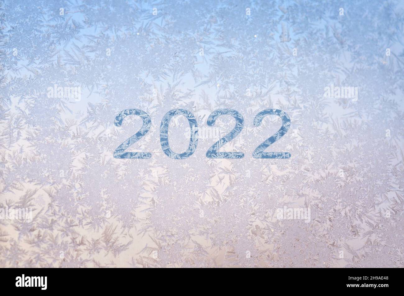 Inscripción de 2022 en el hielo helada sobre el cristal en un fondo de invierno rosa-azul con espacio de copia. El concepto de Feliz Año Nuevo saludos. Foto de stock