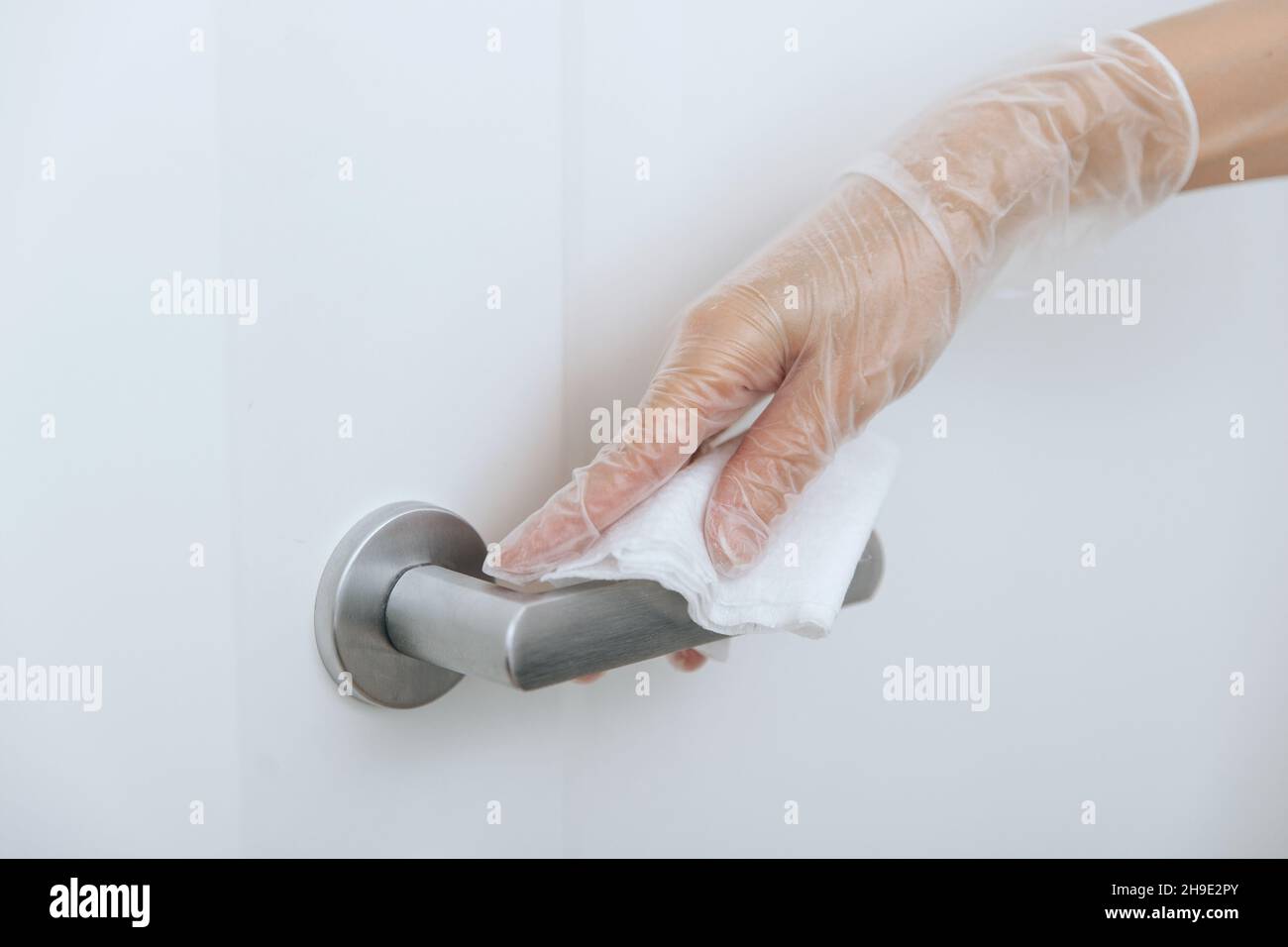 Limpieza de los tiradores de las puertas con toallitas húmedas y guantes blancos. Mano mujer usando toalla para limpiar el enlace de la puerta de la habitación de casa. Desinfecte la prevención de superficies en Foto de stock