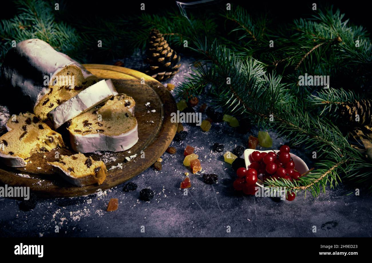 Composición de Año Nuevo. Stollen en una bandeja de madera, fruta confitada, pasas y bayas de viburnum con ramas de árboles de Navidad sobre un fondo clamped. Foto de stock