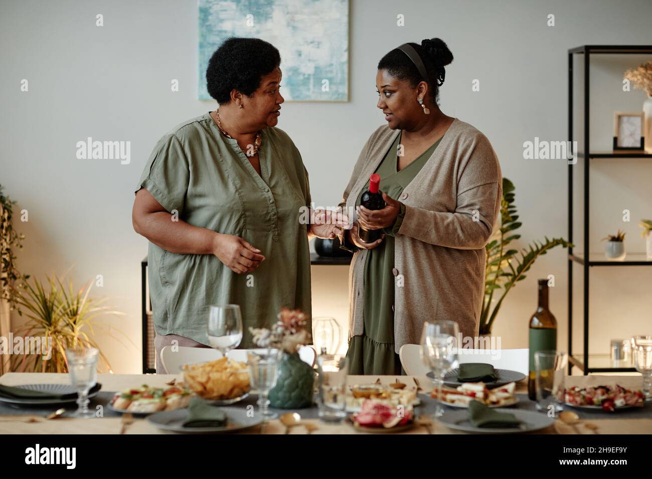 Retrato con cintura de dos mujeres afroamericanas sirviendo mesa para la cena familiar en casa Foto de stock