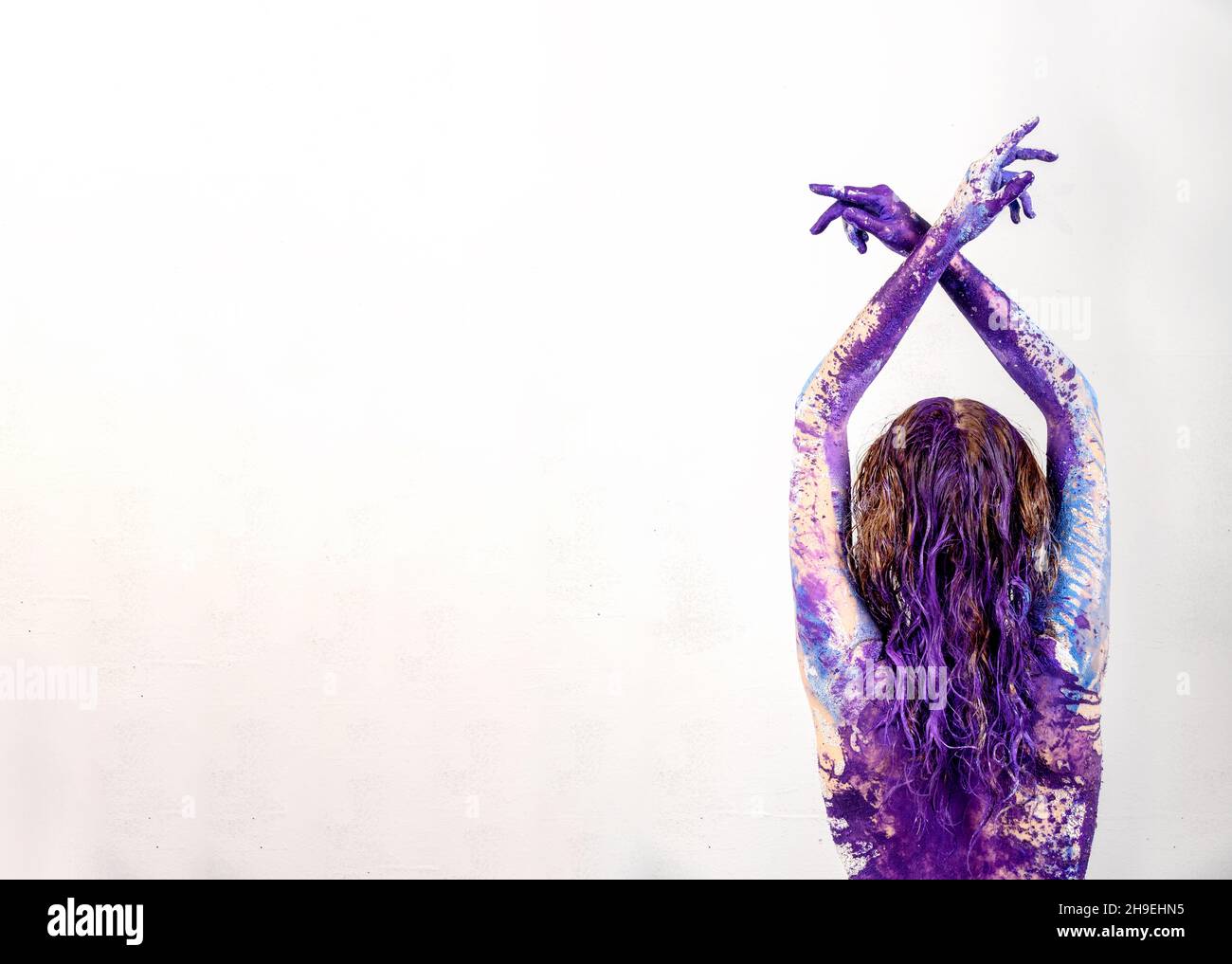 Vista posterior y brazos levantados cruzados de joven mujer artísticamente abstracta pintada, bailarina con blanco, azul y púrpura, pintura violeta, arte creativo del cuerpo Foto de stock