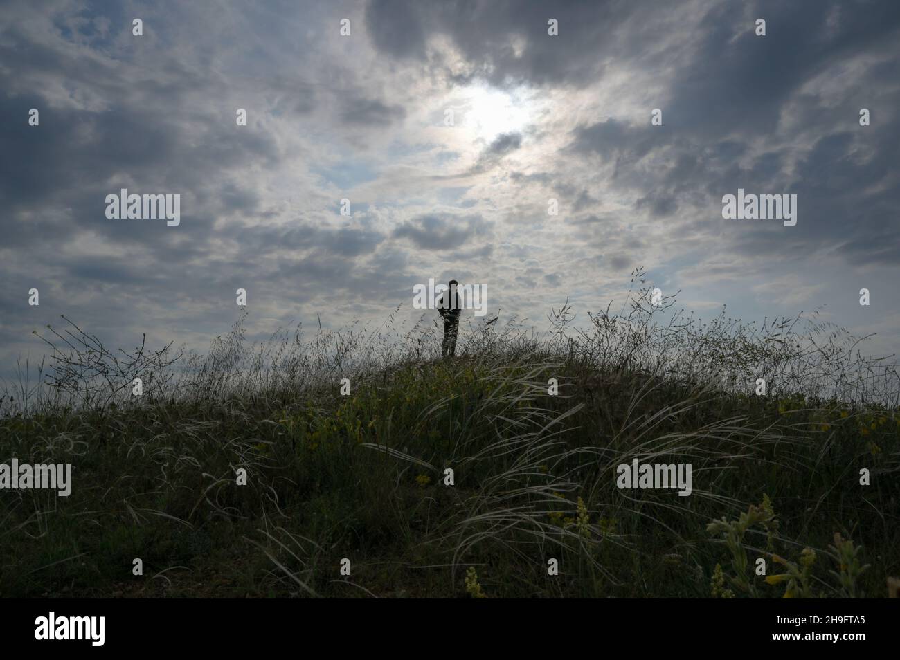solitude concepto de viaje activo masculino en la colina del césped con puesta de sol nublada en el fondo Foto de stock