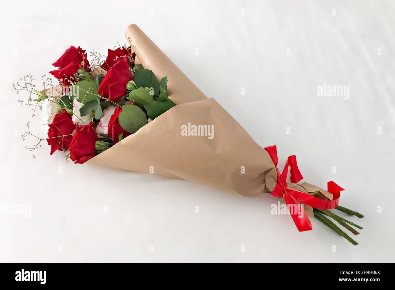 Rosas rojas envueltas en papel kraft marrón y atadas con una cinta roja  sobre un fondo blanco Fotografía de stock - Alamy
