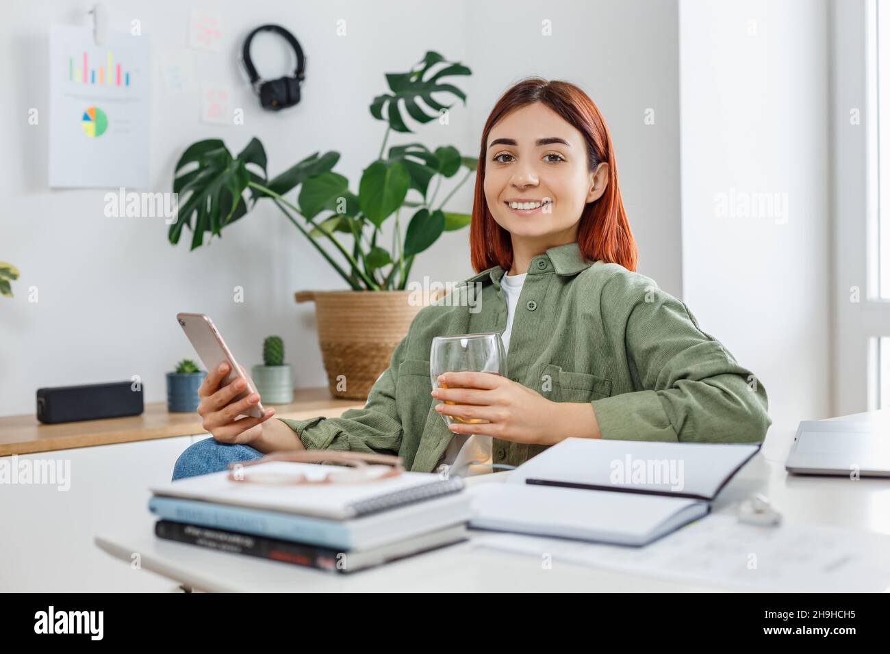 Mujer usando el teléfono móvil y bebiendo té. Joven empresaria en un lugar de trabajo cómodo. Concepto de negocio o comunicación en línea, oficina en casa y. Foto de stock