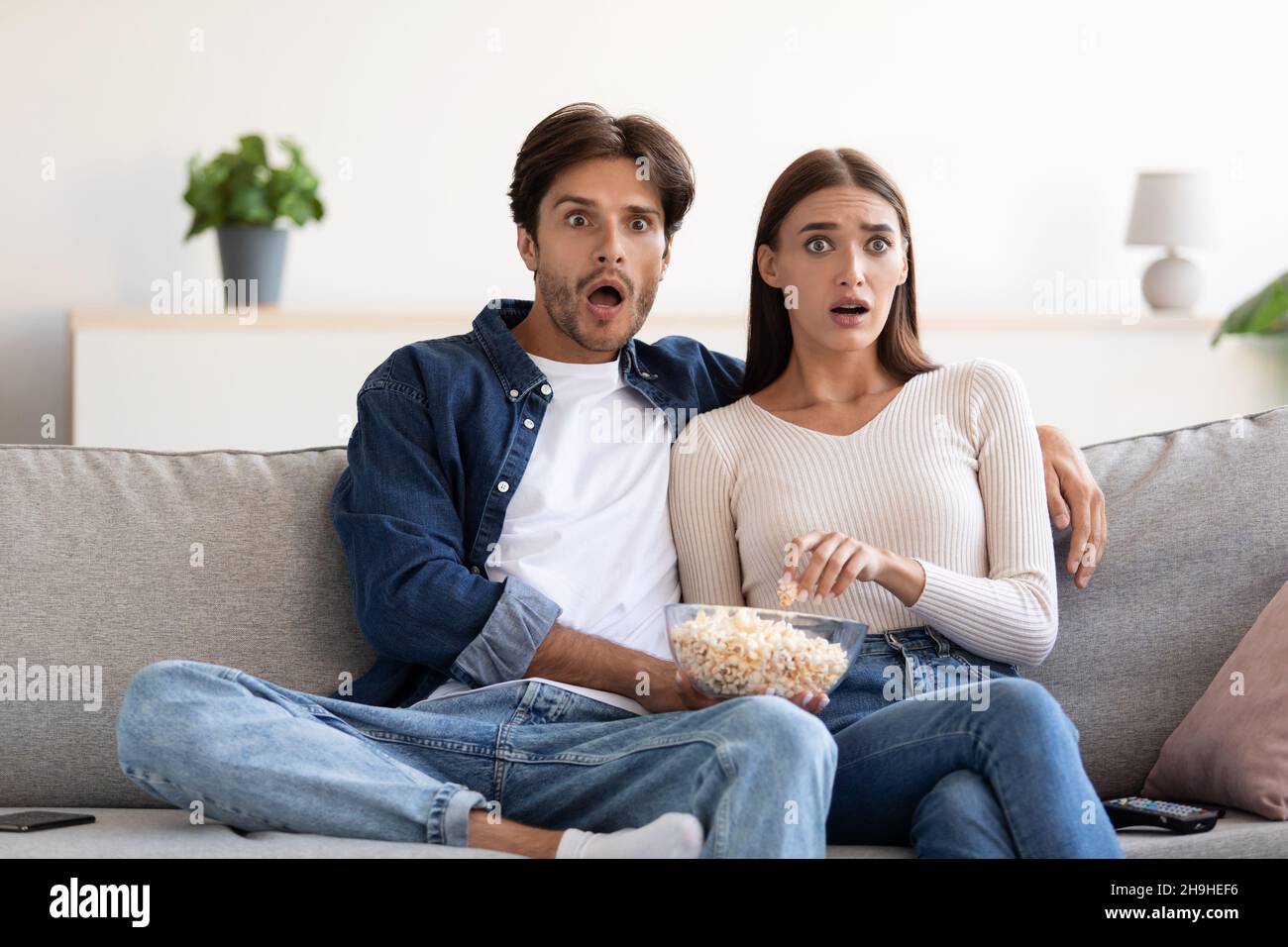 Sorprendida joven pareja europea asustada con boca abierta comiendo palomitas y viendo una película Foto de stock