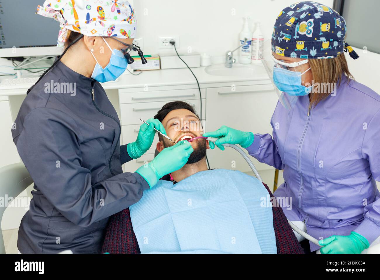 Dentista femenino examina a un paciente hombre en un consultorio dental usando herramientas profesionales y equipo de protección personal. Foto de stock