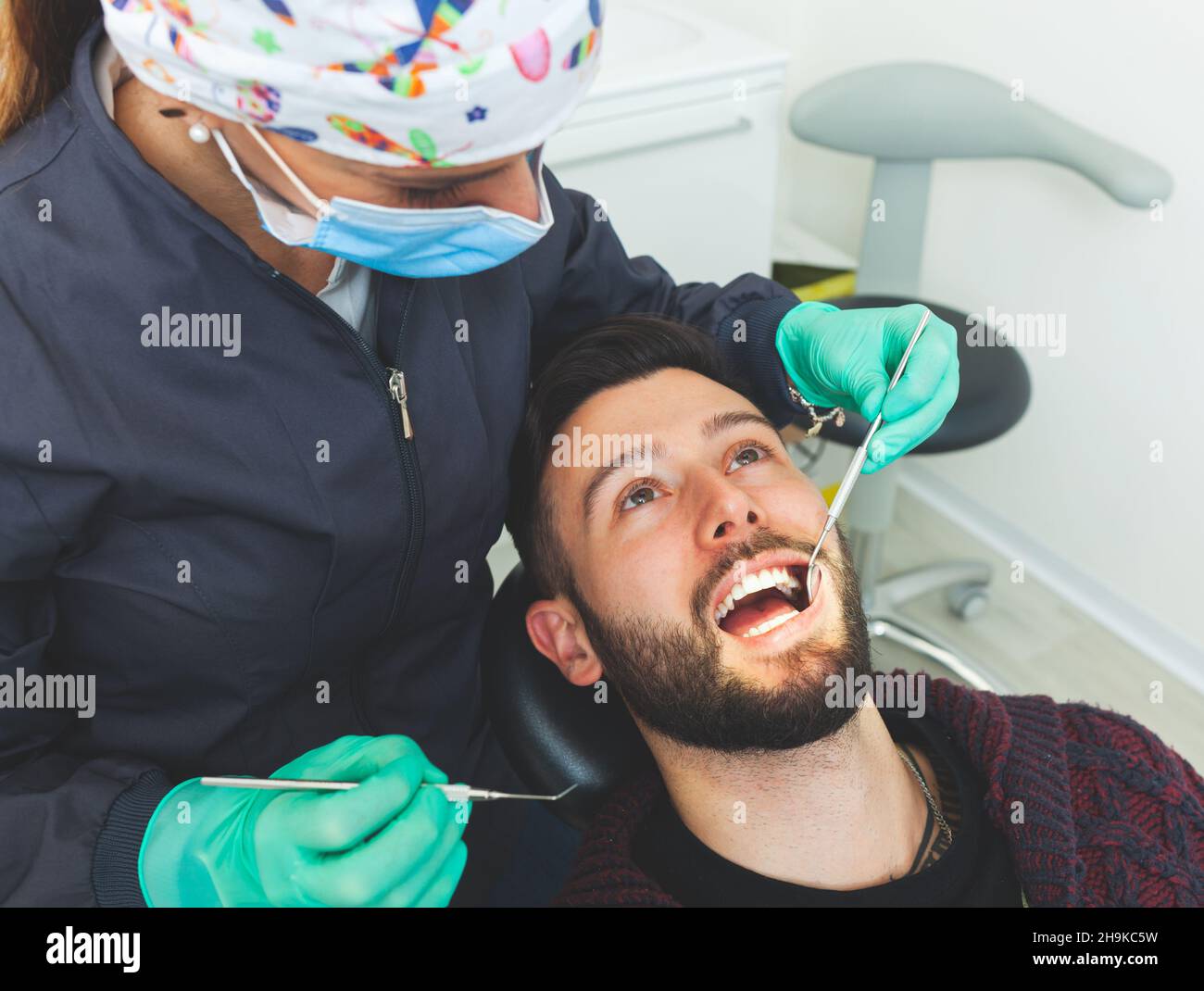 Dentista femenino examina a un paciente hombre en un consultorio dental usando herramientas profesionales y equipo de protección personal. Foto de stock