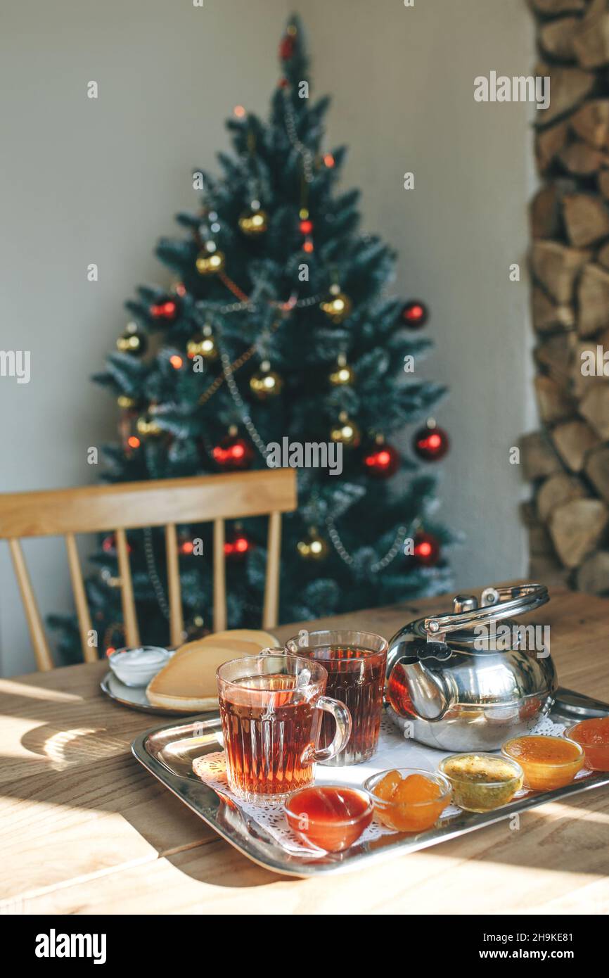Una tetera de té con diferentes tipos de mermelada en el fondo de un árbol de Navidad decorado. El concepto de celebrar y preparar la Navidad y el Año Nuevo Foto de stock