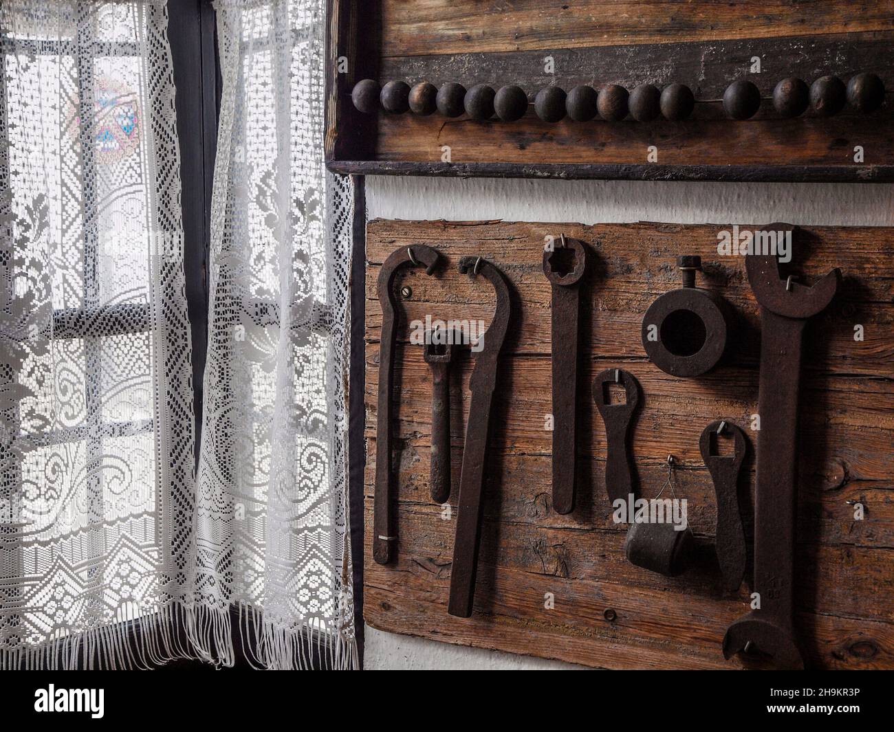 Tabla de madera con herramientas antiguas delante de una ventana con cortinas. Foto de stock