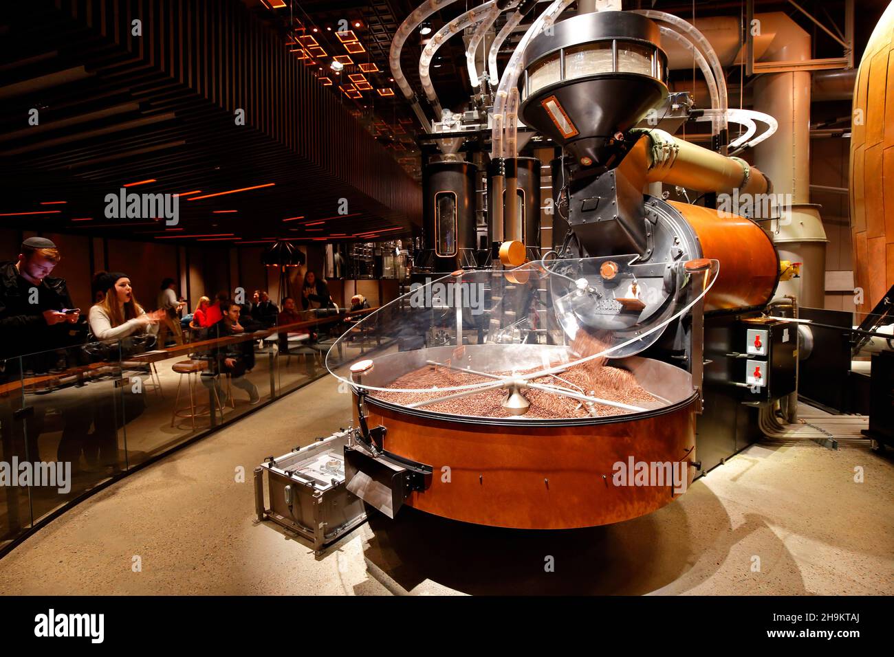 La gente mira los granos de café recién asados que se vierten desde una gran montaña rusa de Probat situada dentro del dominio de la Reserva Starbucks en Nueva York. Foto de stock
