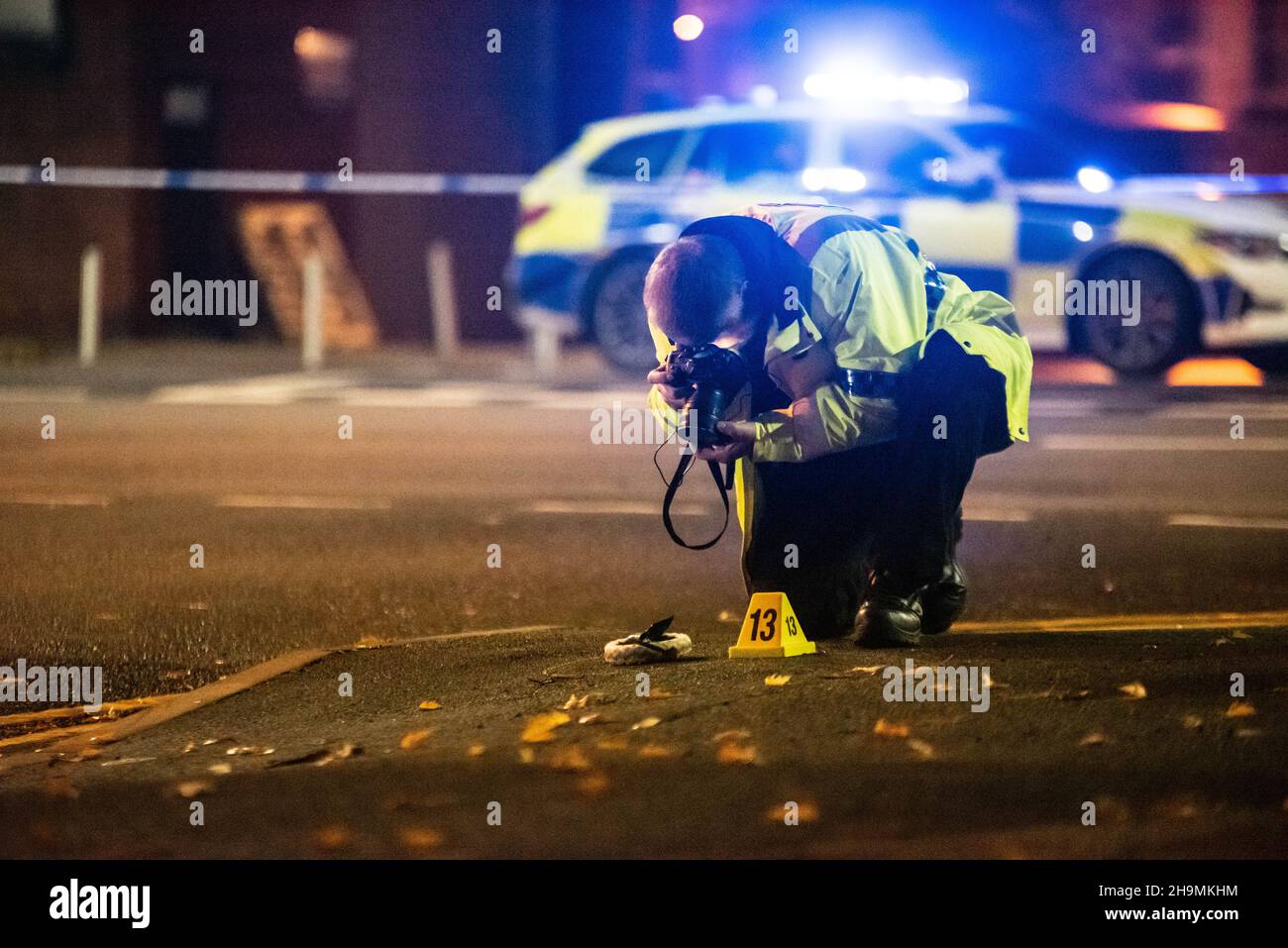 Investigador forense de colisión de la policía de West Midlands, Erdington, Birmingham fotografiando pruebas junto a un cono de evidencia numerado 13. Foto de stock