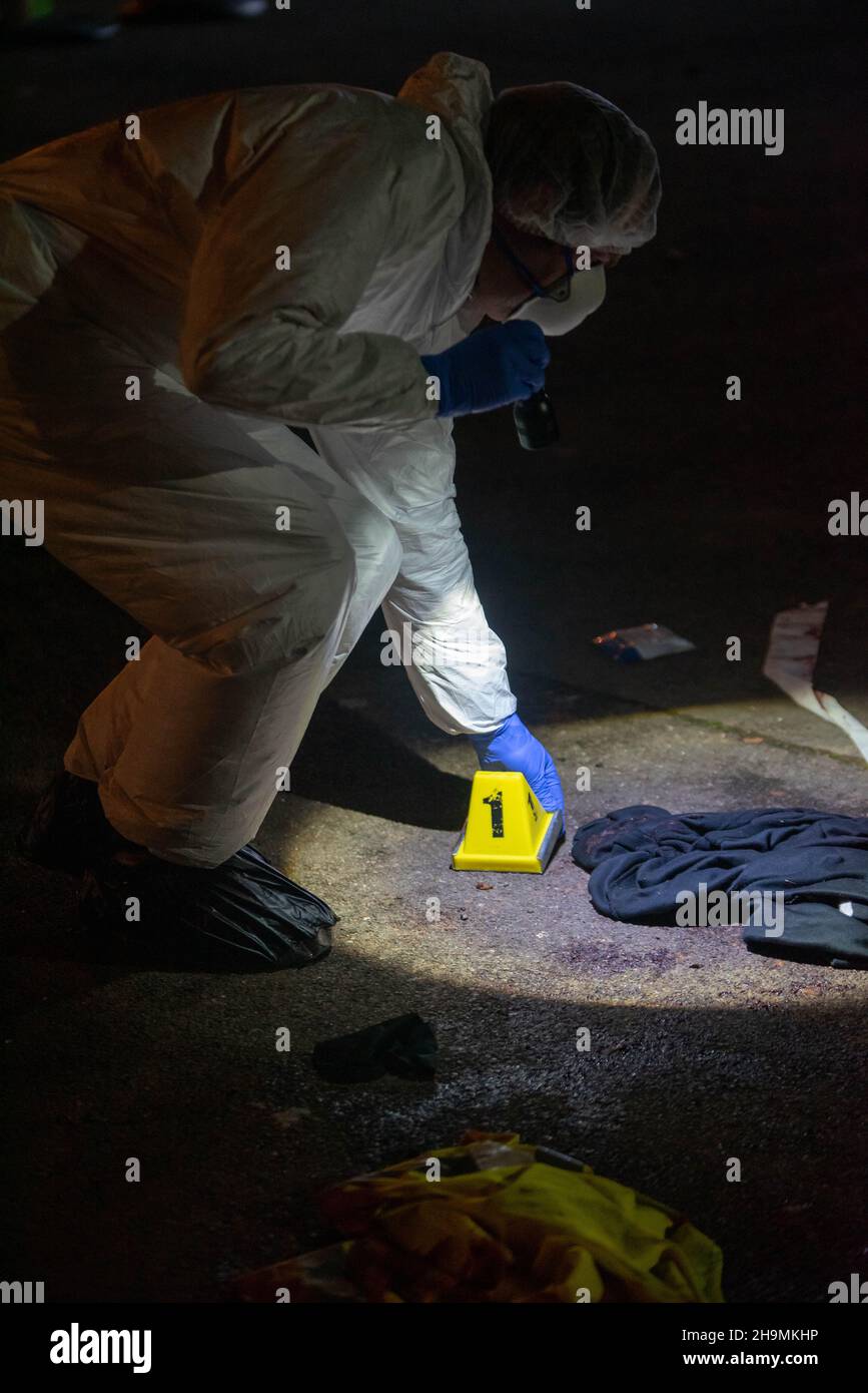 Científico forense colocando un cono de evidencia en la escena de sangre junto a la ropa, Birmingham, Reino Unido Foto de stock