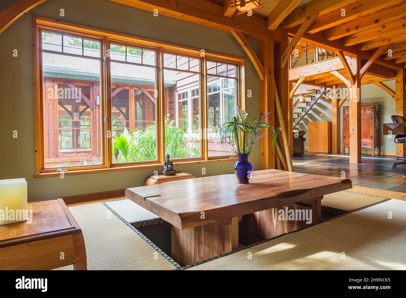 Mesa de comedor de madera rústica barnizada con esteras de tatami y  pequeñas mesas de madera de teca indonesa en un comedor de estilo japonés  dentro de una casa con marco de