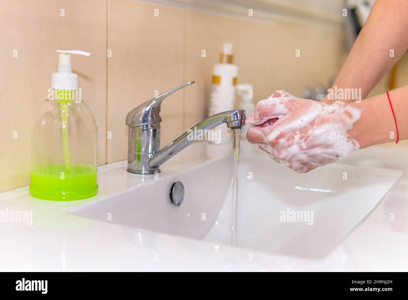 Lávese las manos. Una joven se lava las manos con jabón bajo el grifo sobre un lavabo blanco sobre un fondo negro oscuro. Prevención de virus. Higiénico profesional Foto de stock