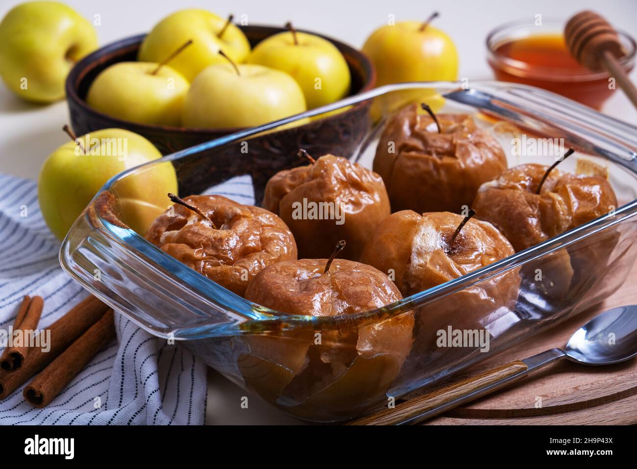 Las manzanas caramelizadas horneadas con miel en un recipiente refractario de cristal se colocan sobre la mesa entre las manzanas amarillas. Enfoque selectivo. Foto de stock