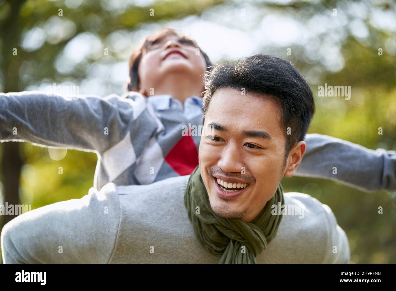 padre asiático llevando a su hijo en la espalda divertirse al aire libre en el parque Foto de stock