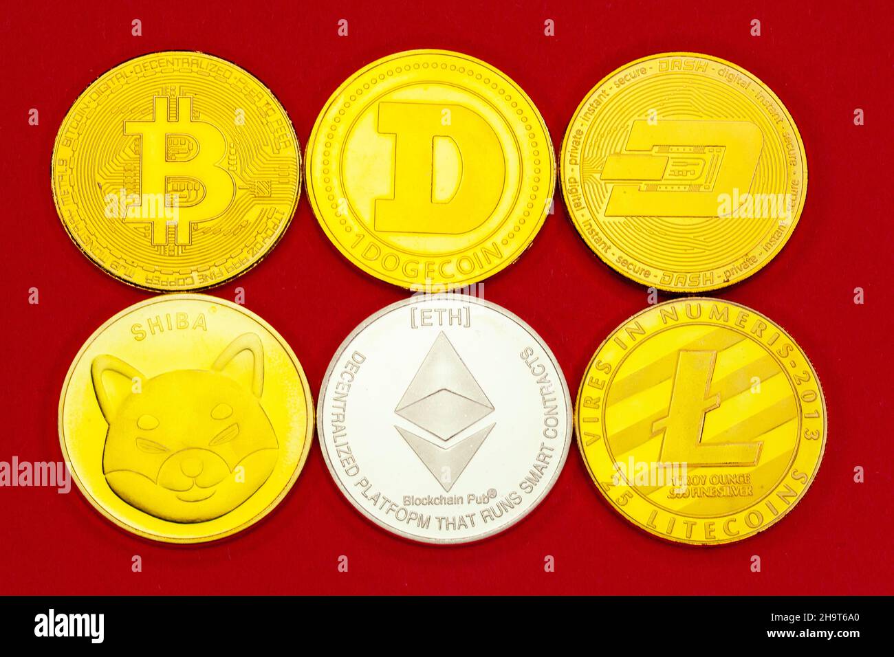 Monedas de criptomoneda Bitcoin, Doge, Dash, Shiba, Ethereum y Litecoin sobre un fondo de estudio rojo. Foto de stock