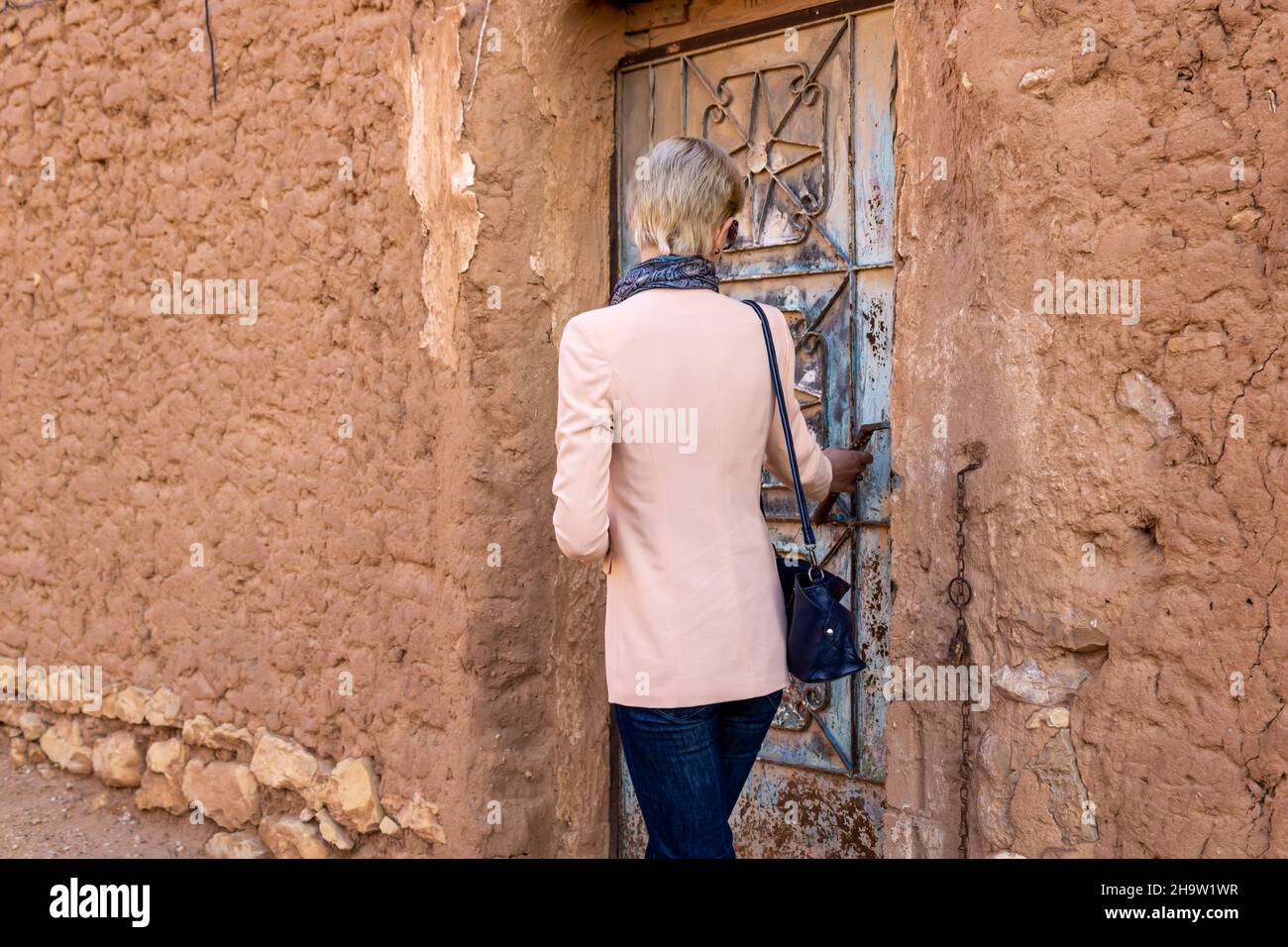 Una turista occidental situada en la antigua puerta de metal de la aldea patrimonial de Ushaiqer, Arabia Saudita. Vista posterior. Foto de stock