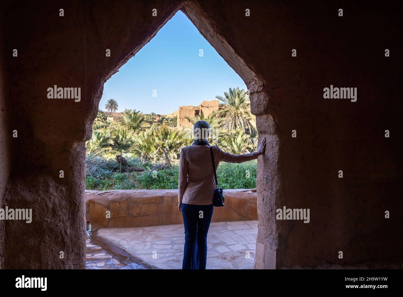 Una solitaria turista occidental que se encuentra bajo el arco en la aldea del patrimonio de Ushaiqer, Arabia Saudita. Vista posterior. Foto de stock