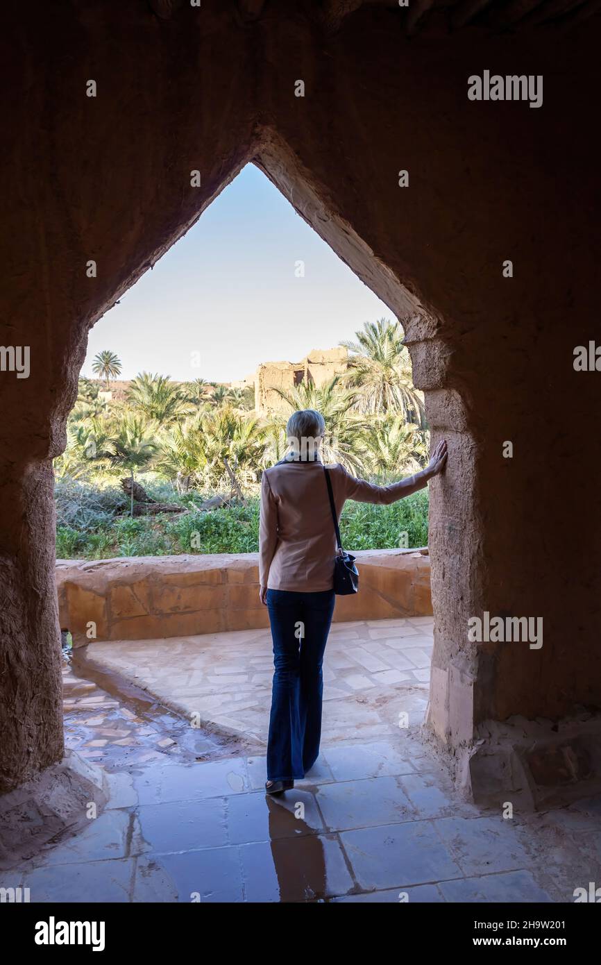 Una solitaria turista occidental que se encuentra bajo el arco en la aldea del patrimonio de Ushaiqer, Arabia Saudita. Vista posterior. Foto de stock