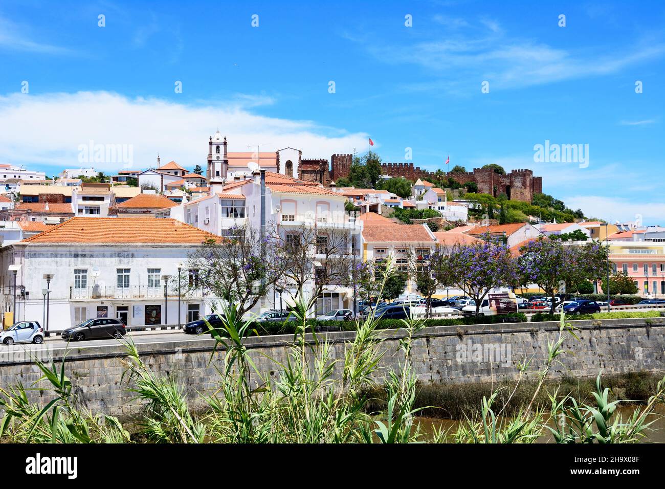 Vista de la ciudad con el castillo y la catedral en la parte trasera y jacarandas en flor en primer plano, Silves, Portugal, Europa. Foto de stock