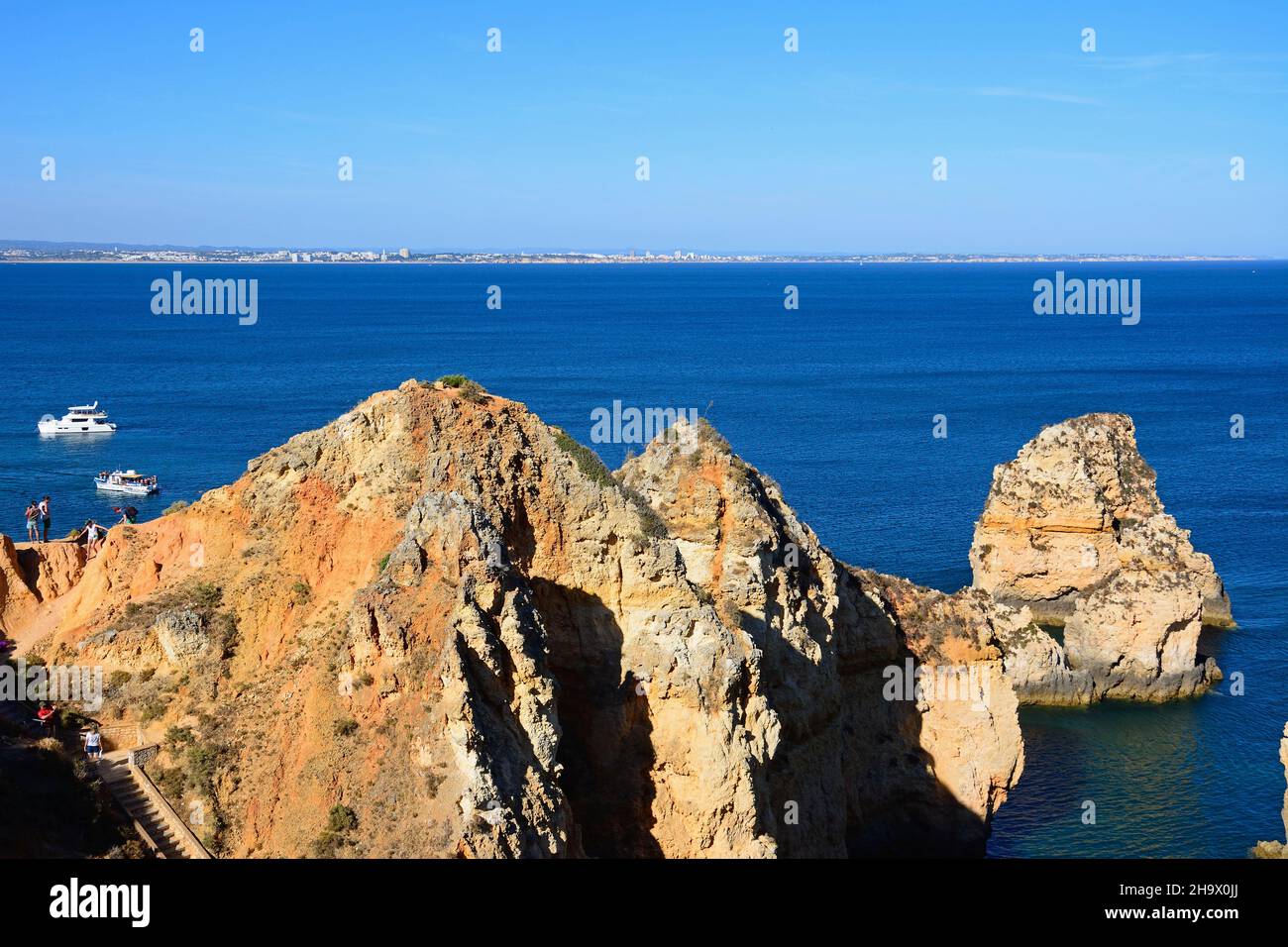 Vista elevada de los turistas que se encuentran en los acantilados con barcos en la bahía, Ponta da Piedade, Lagos, Algarve, Portugal, Europa. Foto de stock