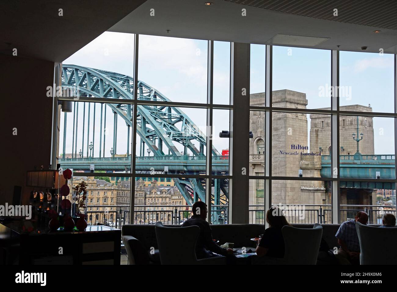 Gente sentada en el bar del hotel Hilton en Gateshead con vista al puente Tyne cruzando el río Tyne, Newcastle upon Tyne, Tyne y Wear, Reino Unido Foto de stock