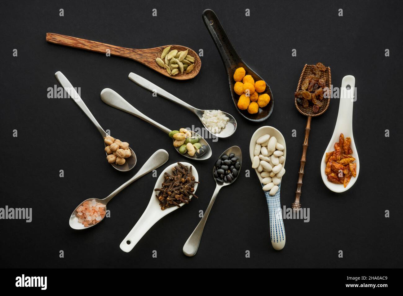 Conjunto de cucharas desordenadas de diferentes materiales y formas llenas  de nueces, semillas, especias y legumbres sobre fondo negro Fotografía de  stock - Alamy