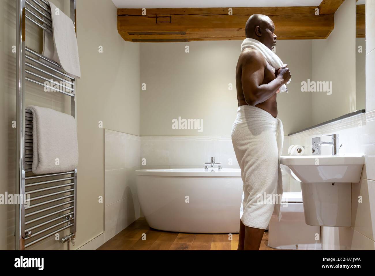 Hombre de etnia africana envuelto en una toalla, en un baño moderno Foto de stock