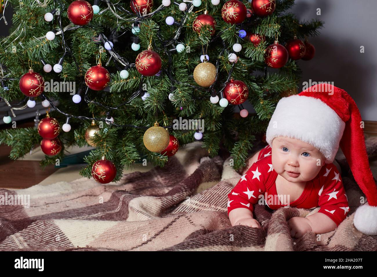 Lindo bebé se arrastra bajo el árbol de Navidad en casa Fotografía de stock  - Alamy