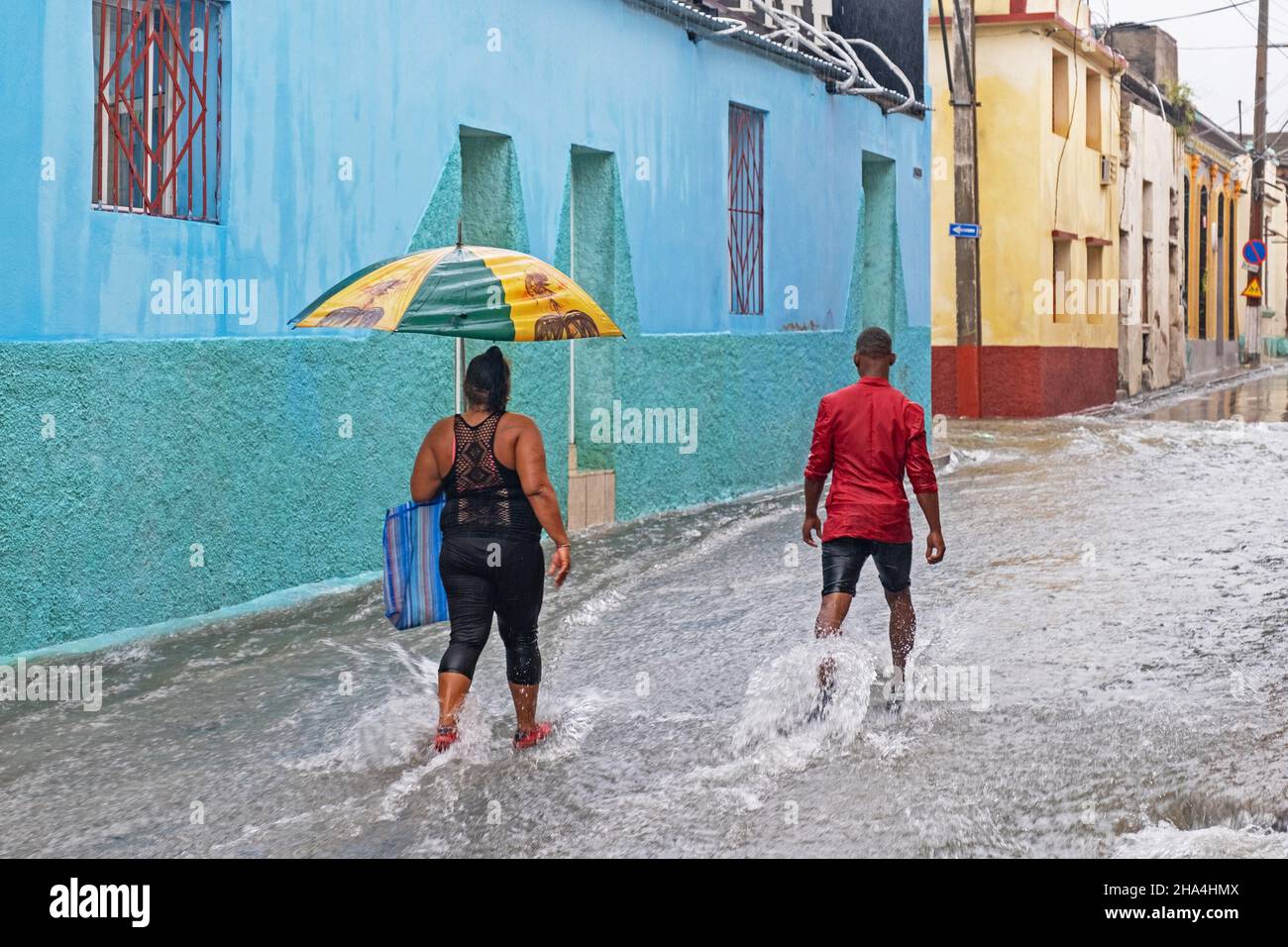 Cubanos con paraguas caminando en la calle inundada durante la lluvia torrencial en la ciudad Santiago de Cuba en la isla Cuba, Caribe Foto de stock