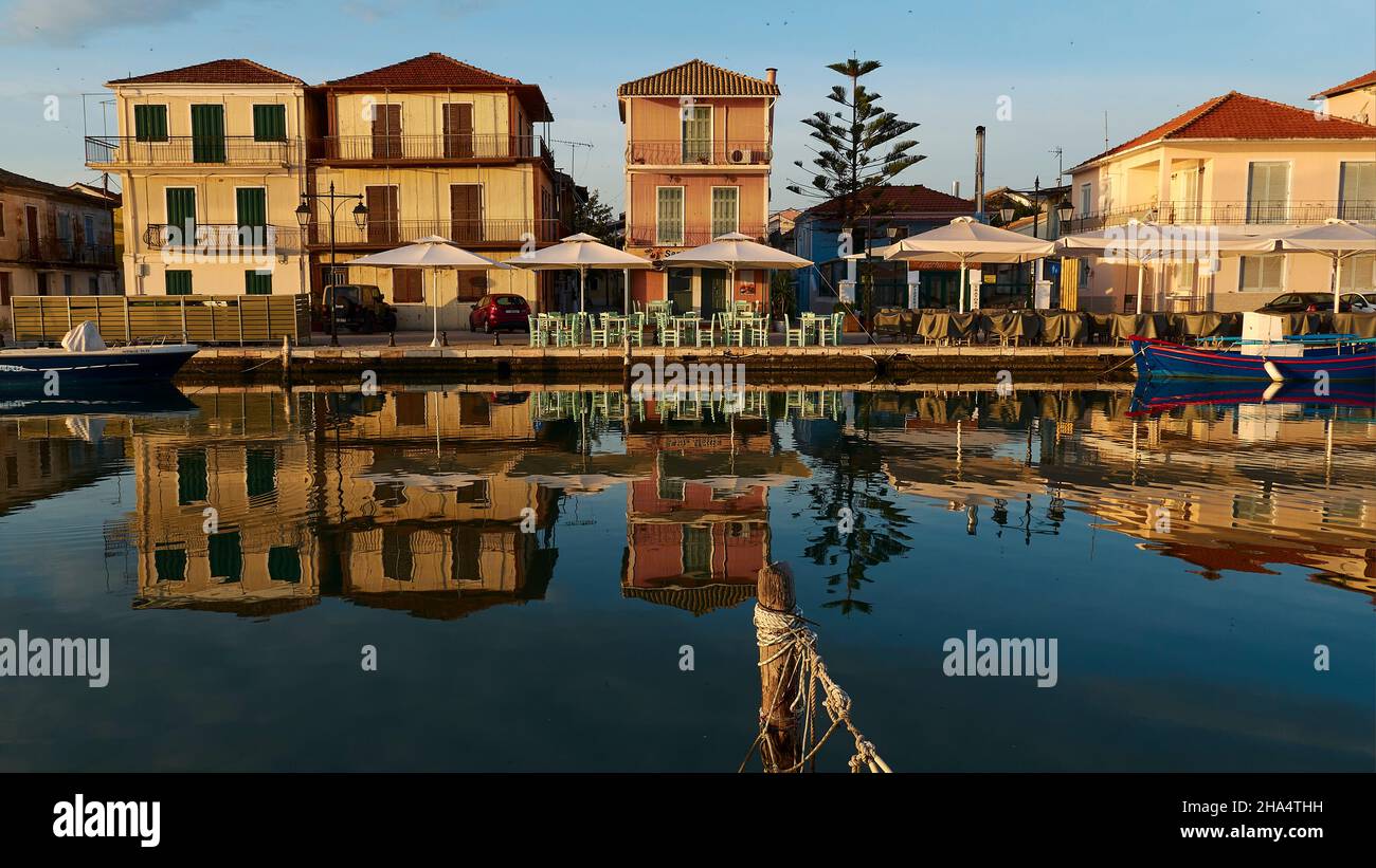 grecia,islas griegas,islas jónicas,lefkada o lefkas,ciudad de lefkada,capital,luz de la mañana,amanecer,fila de casas frontally del frente,reflejado en el agua tranquila del canal,poste de madera en el primer plano Foto de stock