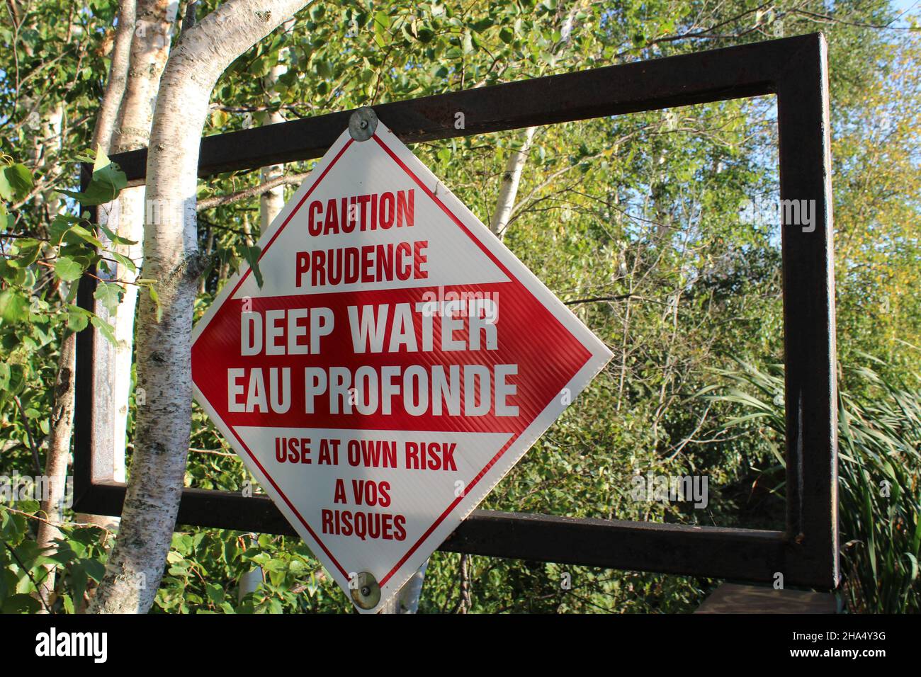 Señal advirtiendo aguas profundas frente a los árboles. Foto de stock