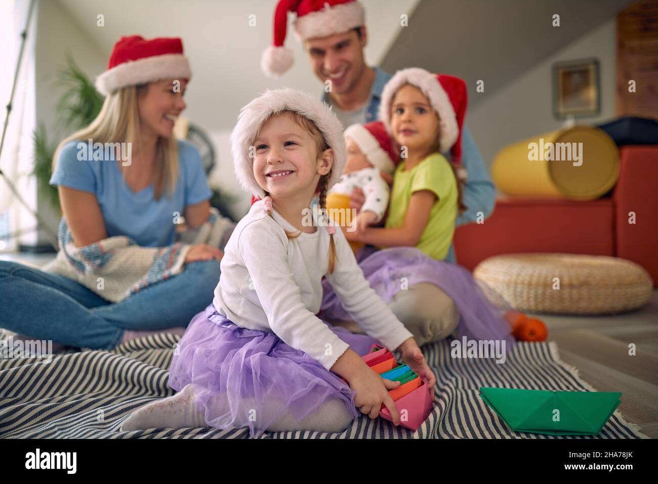 Una familia joven con gorras navideñas está sentada en el suelo junto durante las vacaciones de Navidad en un ambiente festivo en casa. Navidad, hogar, familia Foto de stock