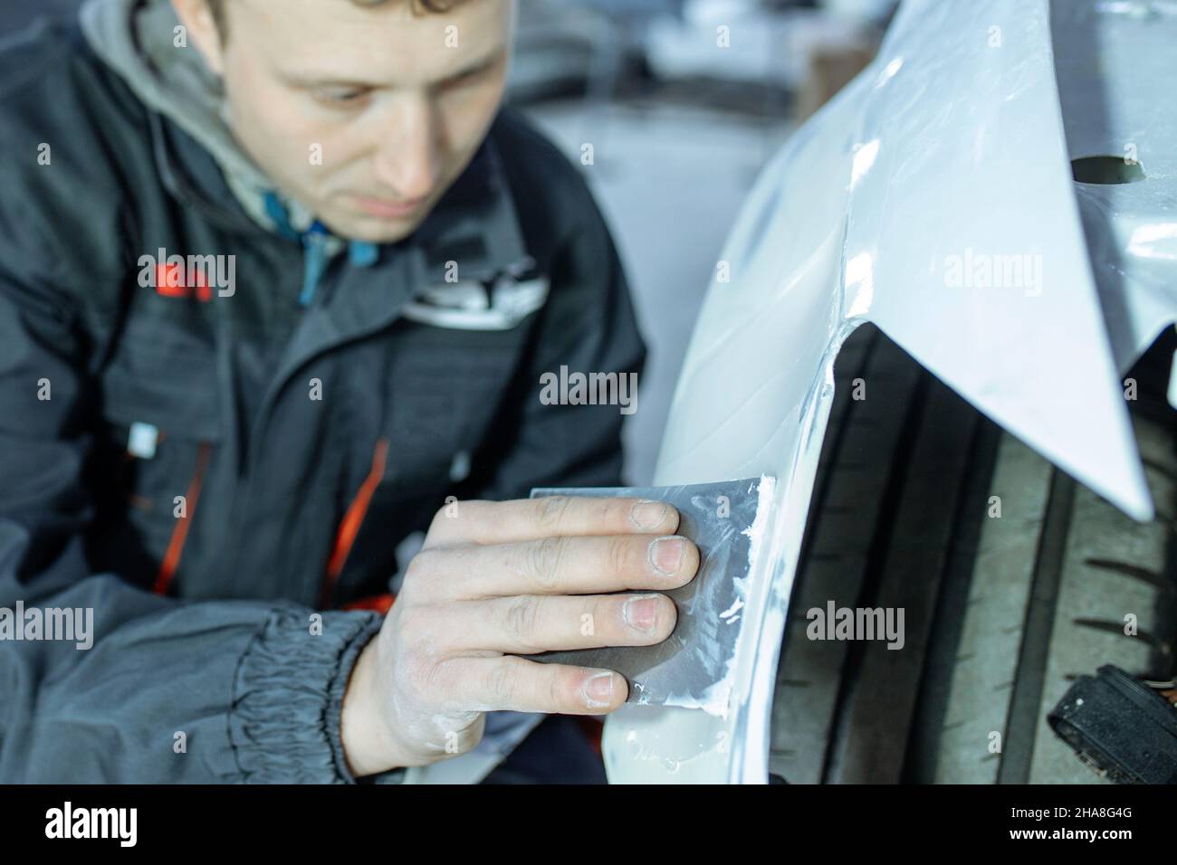 Reparación de la carrocería del automóvil colocando masilla en el trabajo  de cerca después del accidente trabajando con imprimación de lijado antes  de pintar. , el mecánico repara el automóvil, con masilla