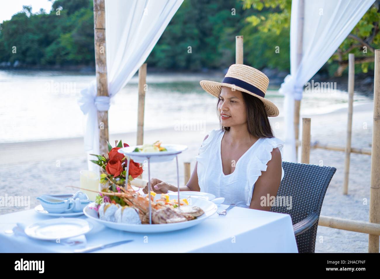 Cena romántica en la playa en Phuket Tailandia, mujer asiática de mediana edad cenando en la playa en Tailandia durante la puesta de sol. Foto de stock