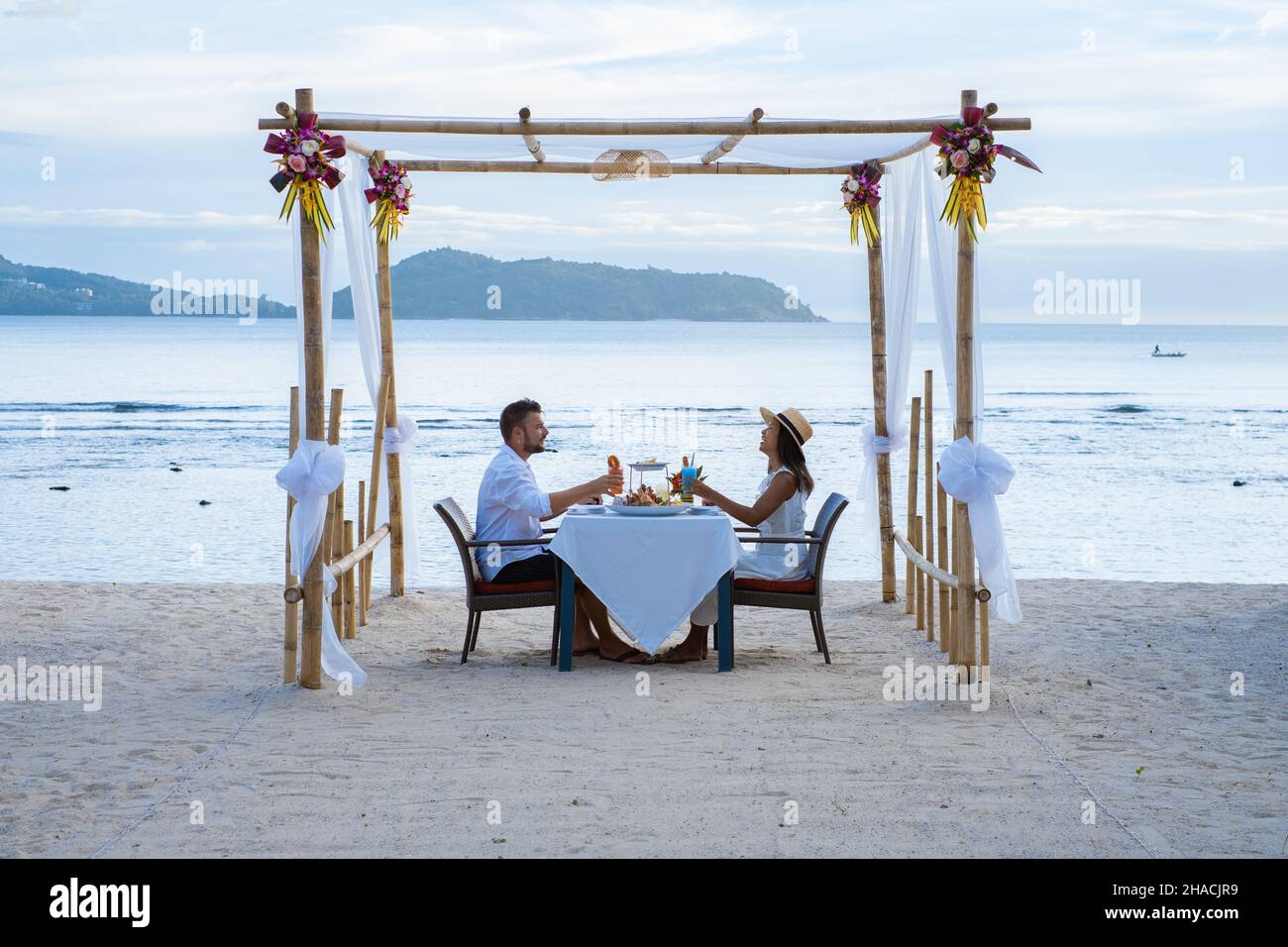 Cena romántica en la playa en Phuket Tailandia, pareja hombre y mujer de mediana edad mujer asiática y hombre europeo cenando en la playa en Tailandia durante la puesta de sol. Foto de stock