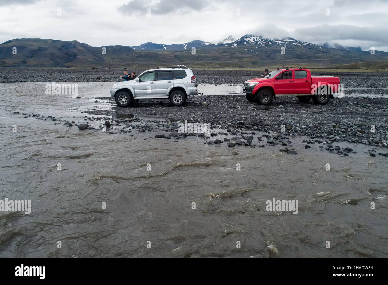 Dos 4WD coches estacionados en las orillas de un río glacial con los conductores fuera discutiendo la mejor manera de cruzar el río sin puente Foto de stock