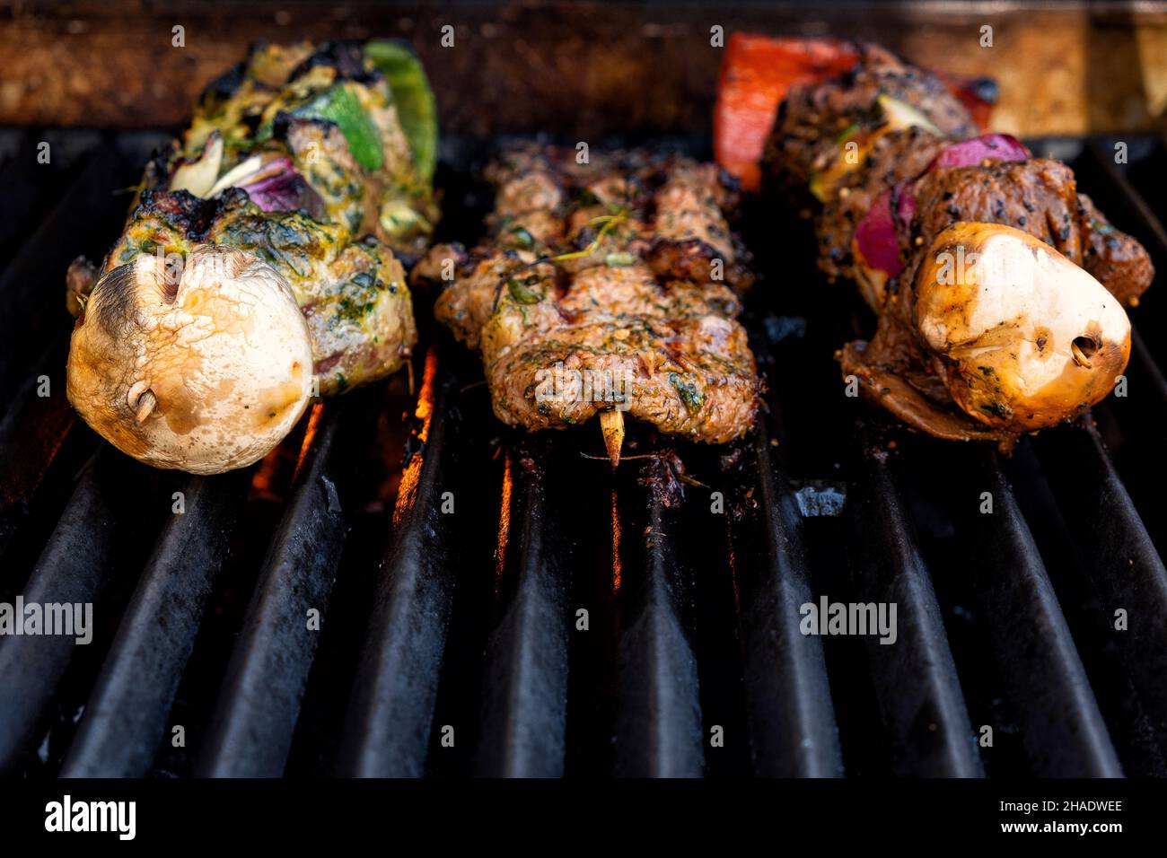 Brochetas de carne a la parrilla preparadas en una parrilla de gas a la barbacoa desde el frente Foto de stock