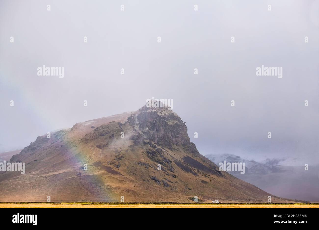 La montaña islandesa rodó en condiciones de niebla con un arco iris que se formó en la base Foto de stock