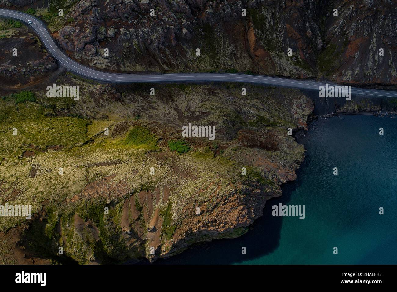Vista aérea de una cadena montañosa en Islandia, terreno de aspecto extranjero con una carretera de asfalto que corre entre una enorme montaña y un lago Foto de stock