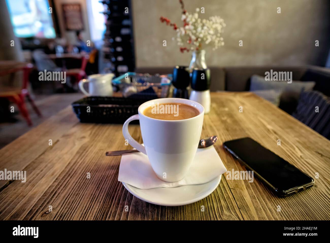 Una taza de café para empezar el día en una cafetería, mesa de madera con smartphone en la parte interior, enfoque poco profundo Foto de stock