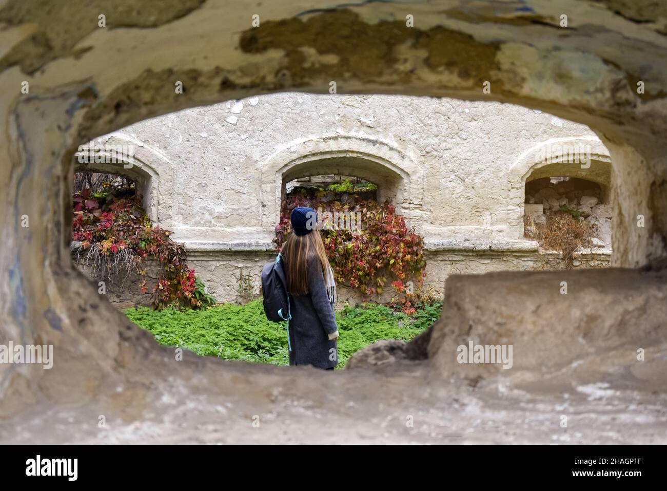 Vacaciones, viajes, turismo en otoño. Chica joven con largo cabello rubio y mochila examina las ruinas de un edificio antiguo. Foto de stock