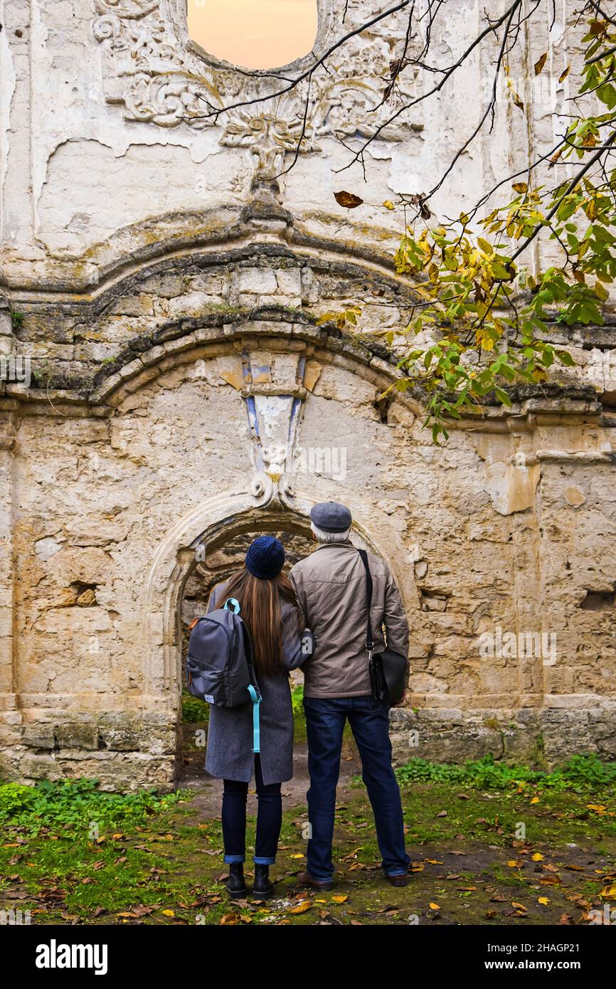 El hombre de pelo gris y la joven chica esbelta con largo cabello rubio examina las ruinas de la antigua sinagoga. Viajero con mochila. Moldavia. Rashkov. Seleccione Foto de stock