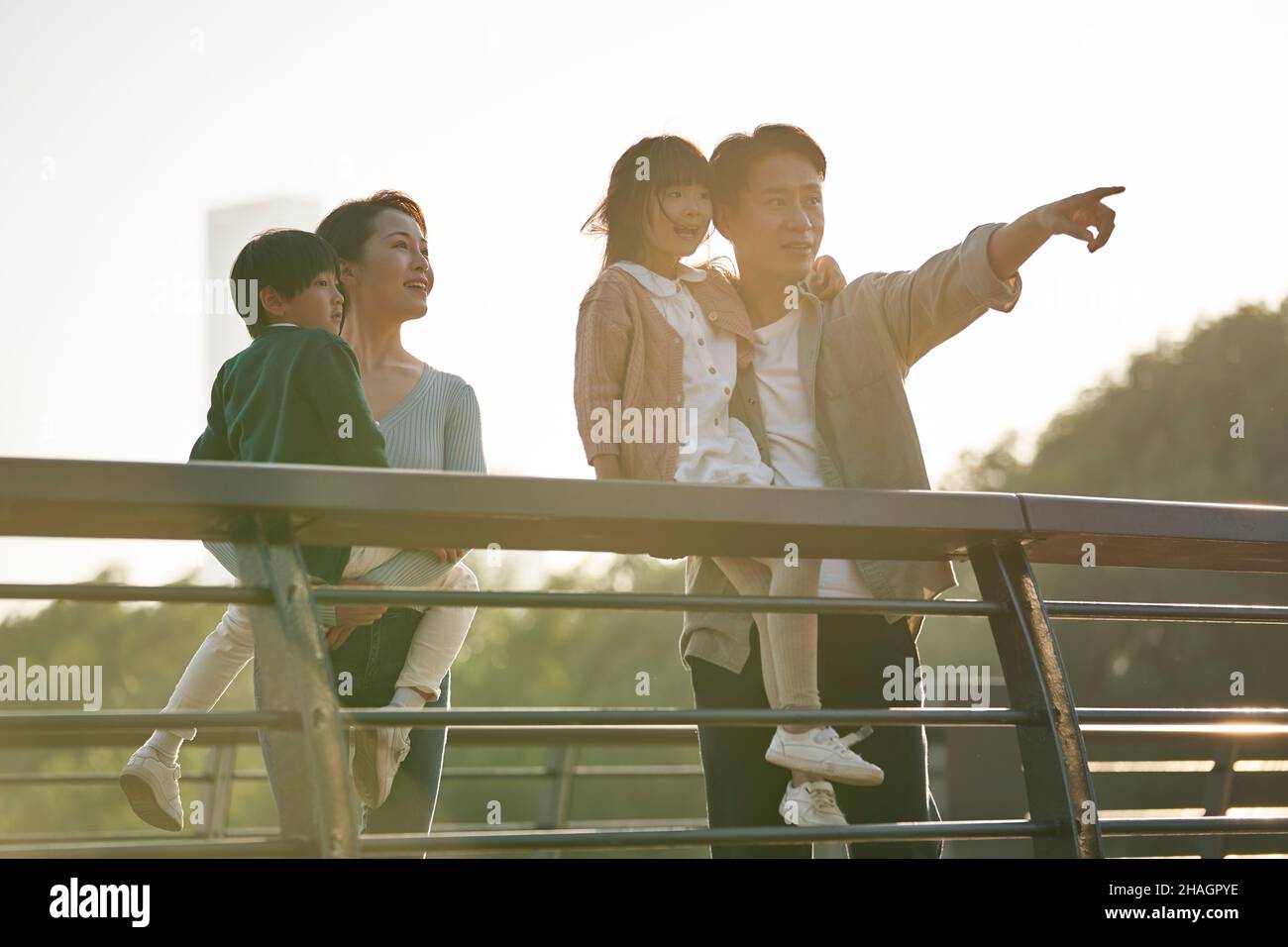 familia asiática con dos niños en un puente peatonal con vistas al parque de la ciudad al atardecer Foto de stock