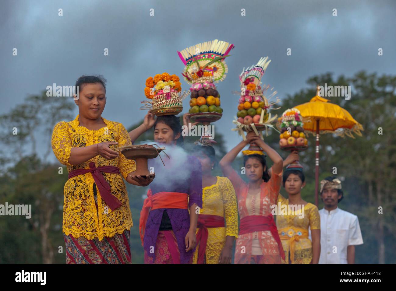 Las mujeres indonesias, tradicionalmente vestidas, llevan frutas y flores cerca del templo y lago de Tamblingan, Bali. Foto de stock