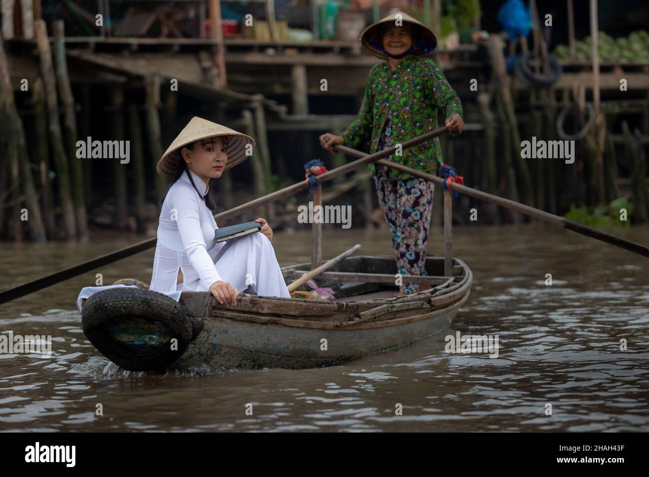 CAN Tho, Vietnam-7 de abril de 2018: Una joven vietnamita vestida tradicionalmente realiza una excursión en barco con una anciana en el río Mekong Foto de stock